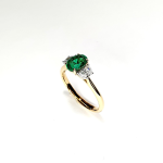 Oval emerald & half moon diamonds three stone ring pictured at an angle facing left.