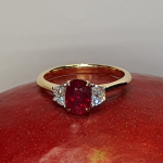 An 18ct yellow gold oval ruby and two half-moon diamond ring with white gold settings on the diamonds is pictured on a red mango, RA00698.