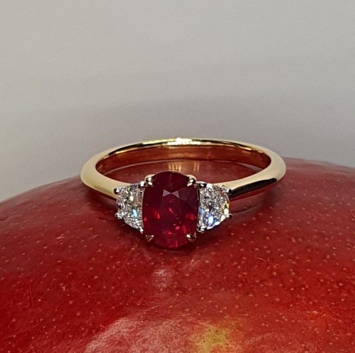 An 18ct yellow gold oval ruby and two half-moon diamond ring with white gold settings on the diamonds is pictured on a red mango, RA00698.
