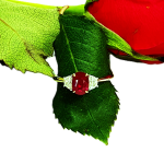 18ct yellow gold three-stone ring with one oval ruby and two half-moon diamonds set in 18ct white gold, one on each side, pictured on a single red rose leaf RA00698.