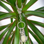 Genuine hallmarked silver tabby cat keyring fob or handbag charm with a grey brown life-like enamelled finish KF00048.Pictuired hanging from a plant.