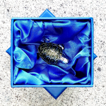 Angled view of the brooch resting in its signature bright blue silk-lined gift box, showcasing premium presentation and packaging.