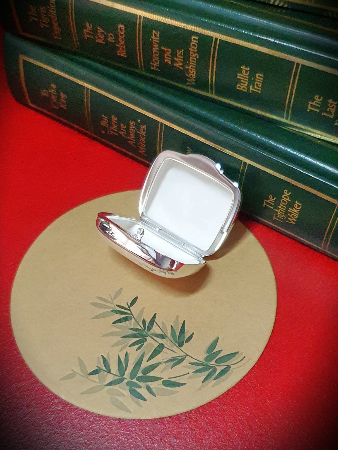 Open pill box placed on bamboo-print mat with books in view Interior details and shape of the open box subtly complemented by natural textures and book-lined background.