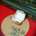 Open pill box placed on bamboo-print mat with books in view Interior details and shape of the open box subtly complemented by natural textures and book-lined background.