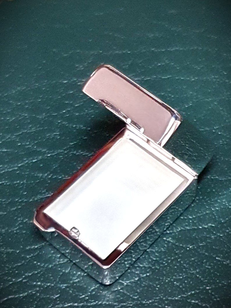 Open hallmarked sterling pill box, tablet shape design with inner compartment visible and matte silver surface captured clearly on green leather back ground.