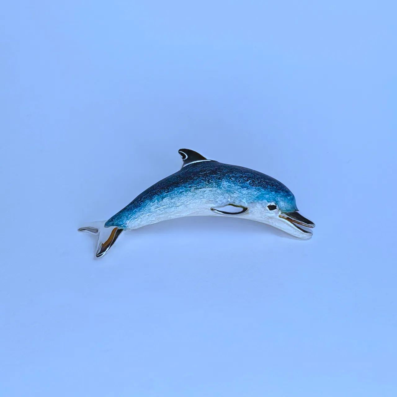 Lifelike enamelled Dolphin brooch made in Italy in genuine hallmarked silver. Pictured on a blue background.