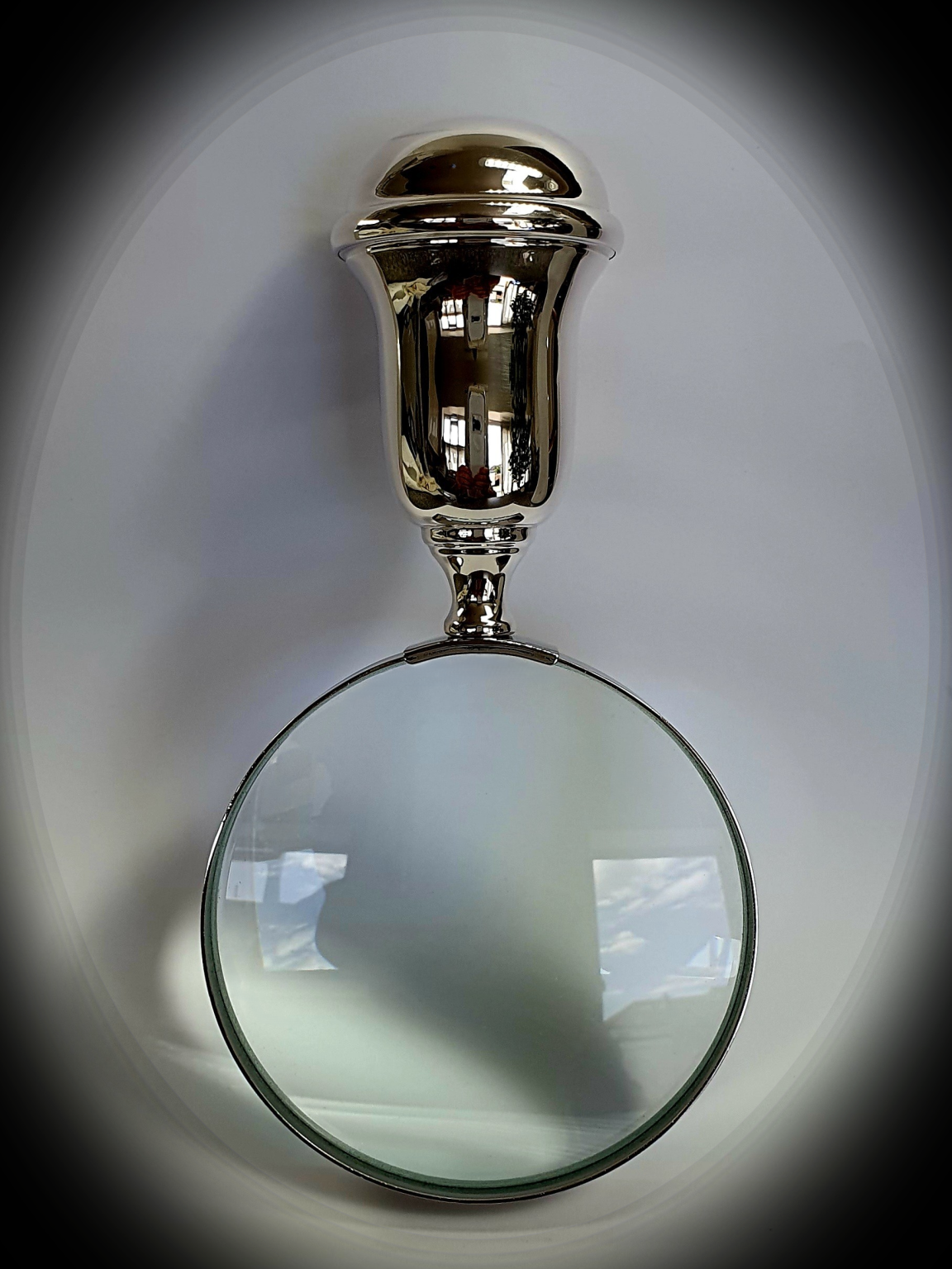 Direct face-on shot of magnifying glass under a subtle spotlight, highlighting the lens curvature and casting a gentle halo on the surface below.