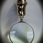 Direct face-on shot of magnifying glass under a subtle spotlight, highlighting the lens curvature and casting a gentle halo on the surface below.