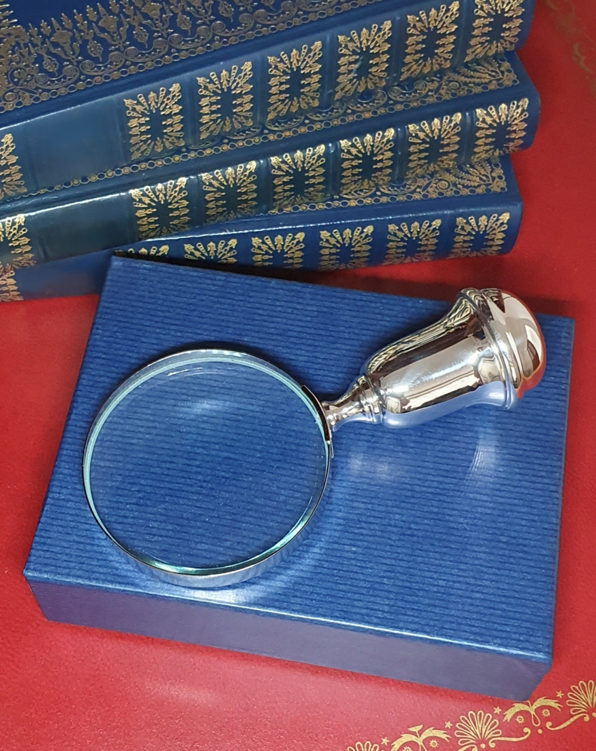 Sterling silver magnifying glass with bulbous handle, resting atop a blue cardboard gift box