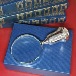 Sterling silver magnifying glass with bulbous handle, resting atop a blue cardboard gift box