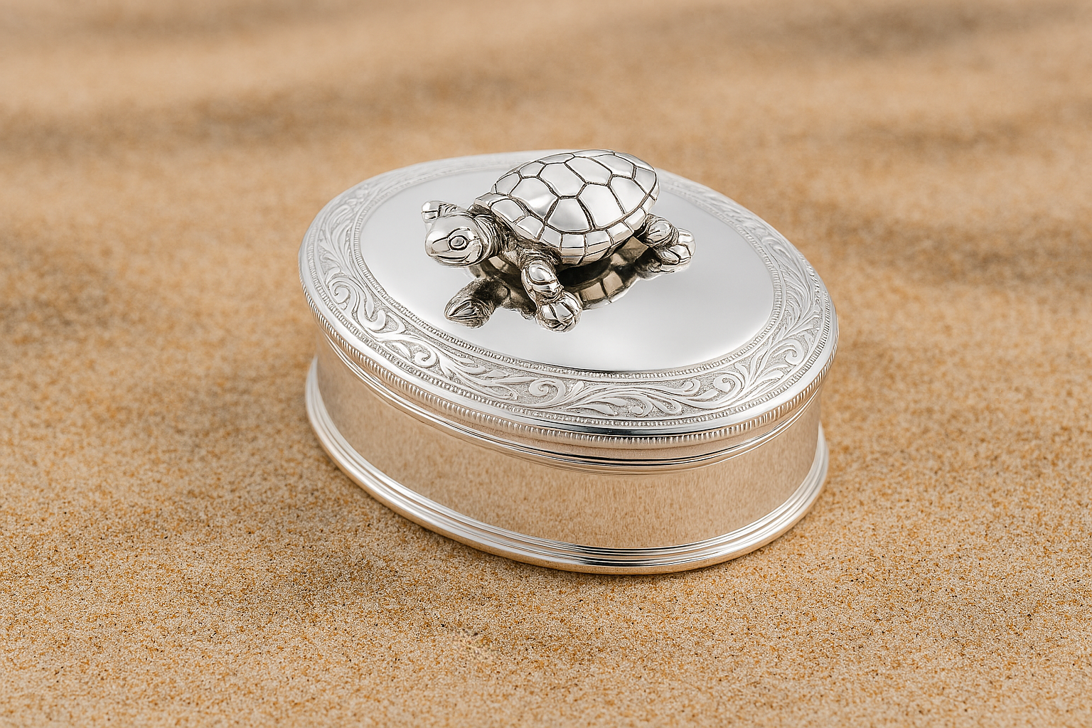 Silver oval pill box with scroll engraving and movable turtle, photographed on soft sand.