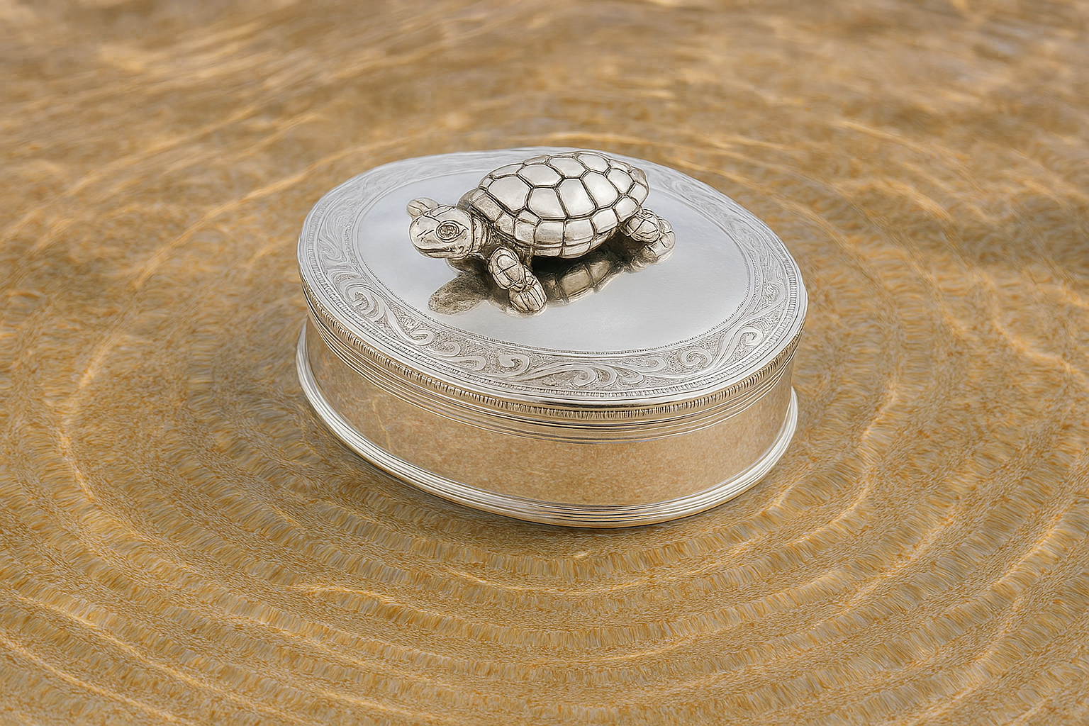 Sterling silver box with scrollwork and movable turtle, placed on sand beside rippling water.