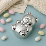 Silver teddy bear pillbox with pastel sweets, baby blanket, and storybook—nostalgic theme.