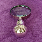 Silver magnifier lying on rich purple fabric, showcasing the rounded end of its ergonomic handle and polished finish.