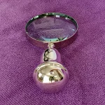 Silver magnifier lying on rich purple fabric, showcasing the rounded end of its ergonomic handle and polished finish.