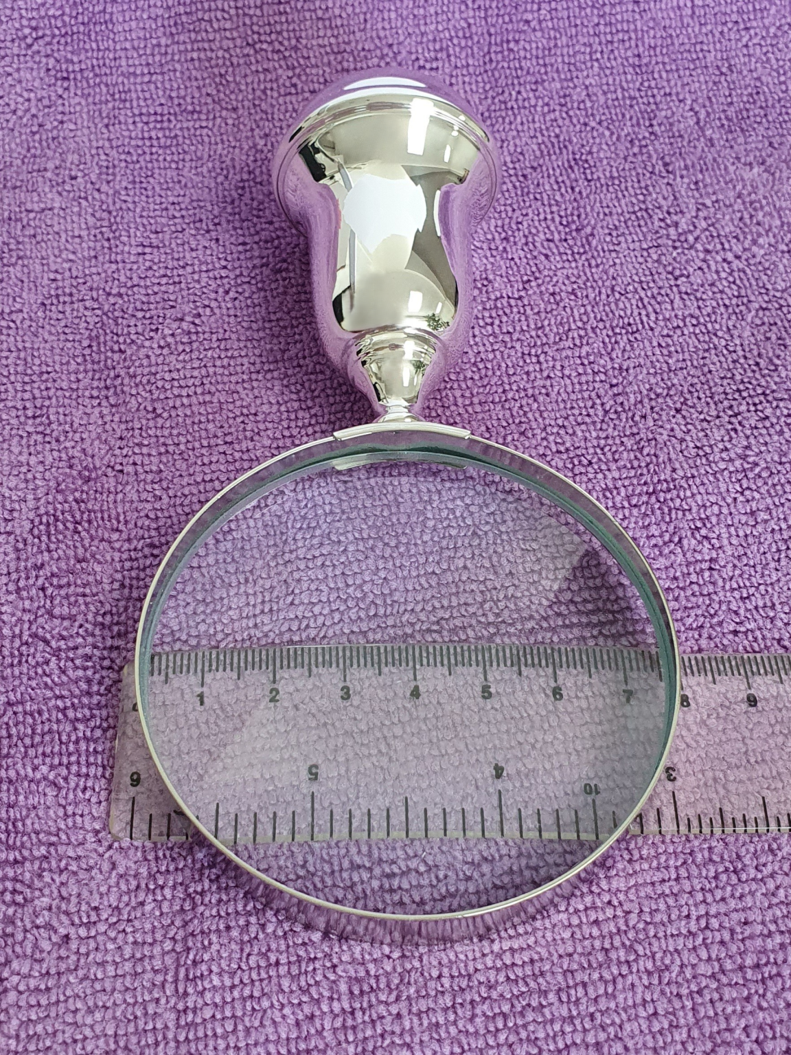 Inspection glass on purple cloth with ruler indicating lens diameter, emphasising clarity and craftsmanship.