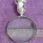 Inspection glass on purple cloth with ruler indicating lens diameter, emphasising clarity and craftsmanship.
