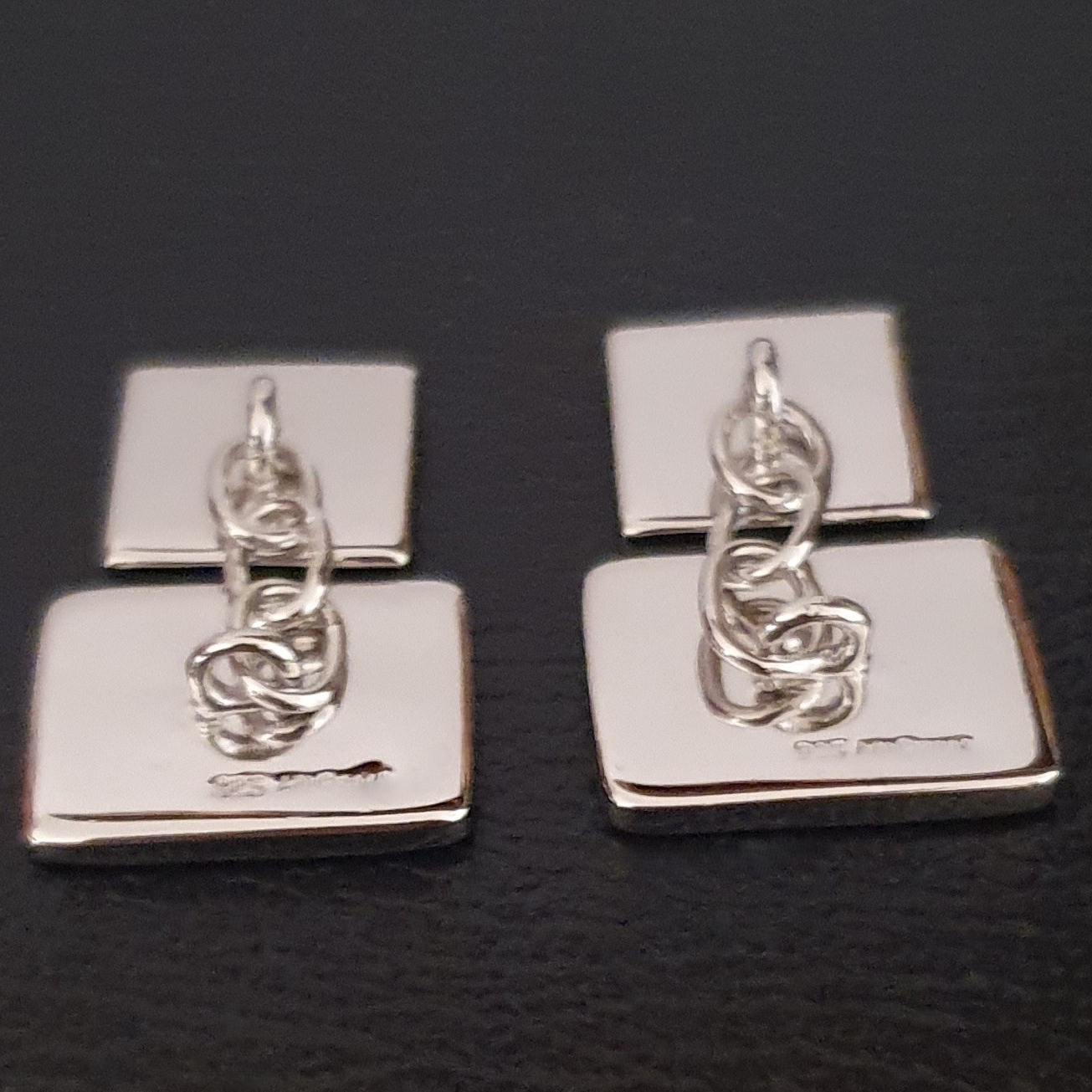 Rear view of cufflinks showing plain sterling silver backs with attached chain links.