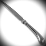 Sterling silver pistol grip letter opener displayed under spotlight with dark vignette and bright centre.