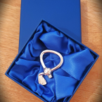 The real silver golf club and ball key ring rests in a deep blue presentation box lined with soft blue silk. The left‑facing angle and rich fabric texture enhance the shine of the club and the detailed ball.