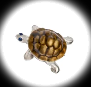 Close‑up of a single sterling silver tortoise cufflink with vitreous enamel shell and sapphire eye, shown on a black background with a soft white spotlight effect highlighting the details.