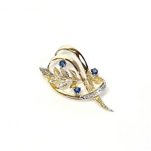 9ct yellow gold brooch with a sprig of seven leaves coming through a floral swirl of polished and barked yellow gold with three diamonds set into a small white rhodium section 