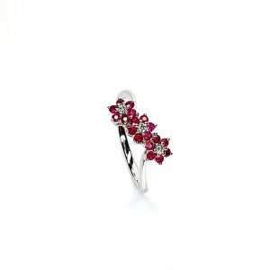 A captivating image of a Three Cluster Ruby Ring in 18ct white gold. The ring showcases three clusters of vibrant rubies, with six rubies in each cluster. Adorning the ring shank is a graceful wave design, adding a touch of elegance to the overall aesthetic. The clusters are accentuated by three sparkling diamonds, positioned at the centre of each cluster." Angled top view.